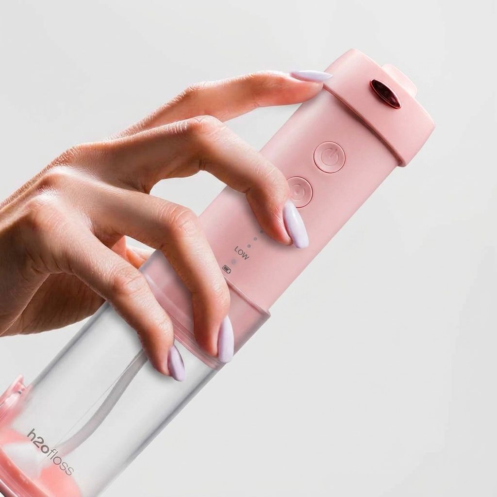 Pink and clear water bottle held by a hand with light nail polish on a light gray background